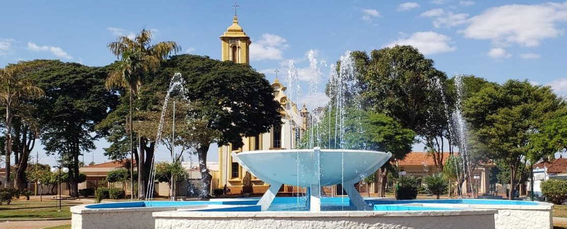 Fonte da Praça Central de Guará com a Igreja Matriz ao fundo, sob céu azul